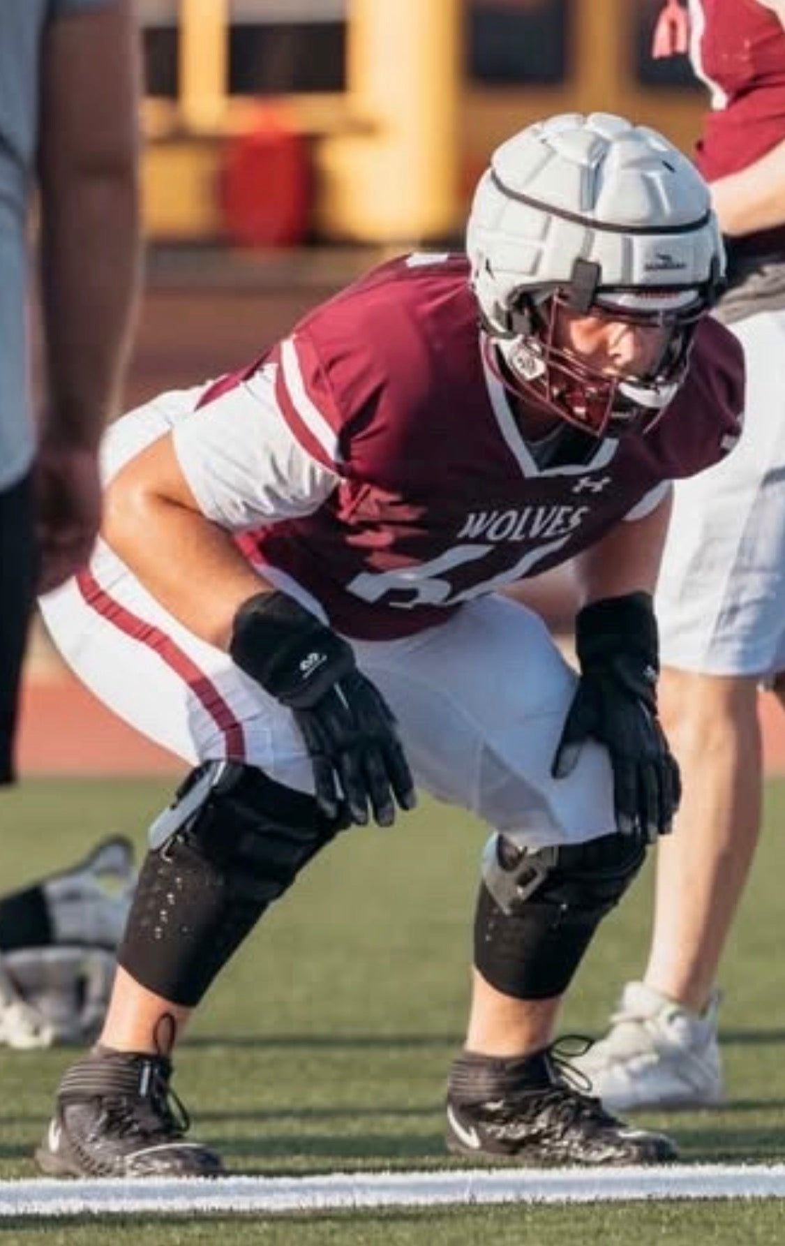 Football lineman in a stance wearing the black AMS Compression Leg Sleeve to keep his knee brace from sliding