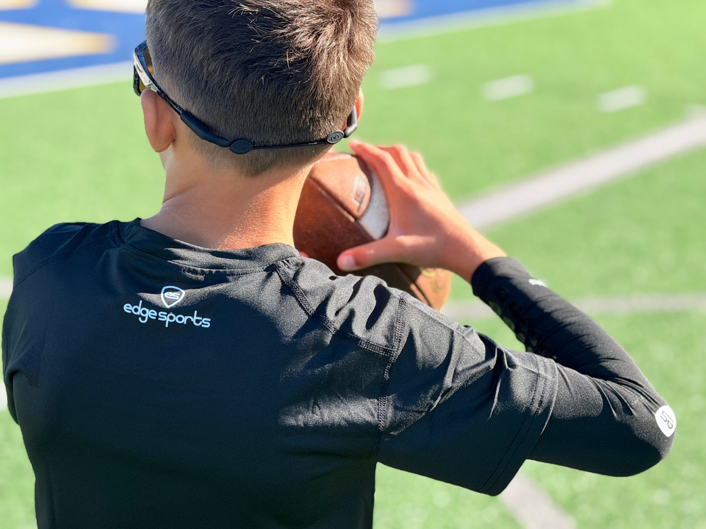 Teen athlete wearing the black compression shirt while throwing the football on the turf
