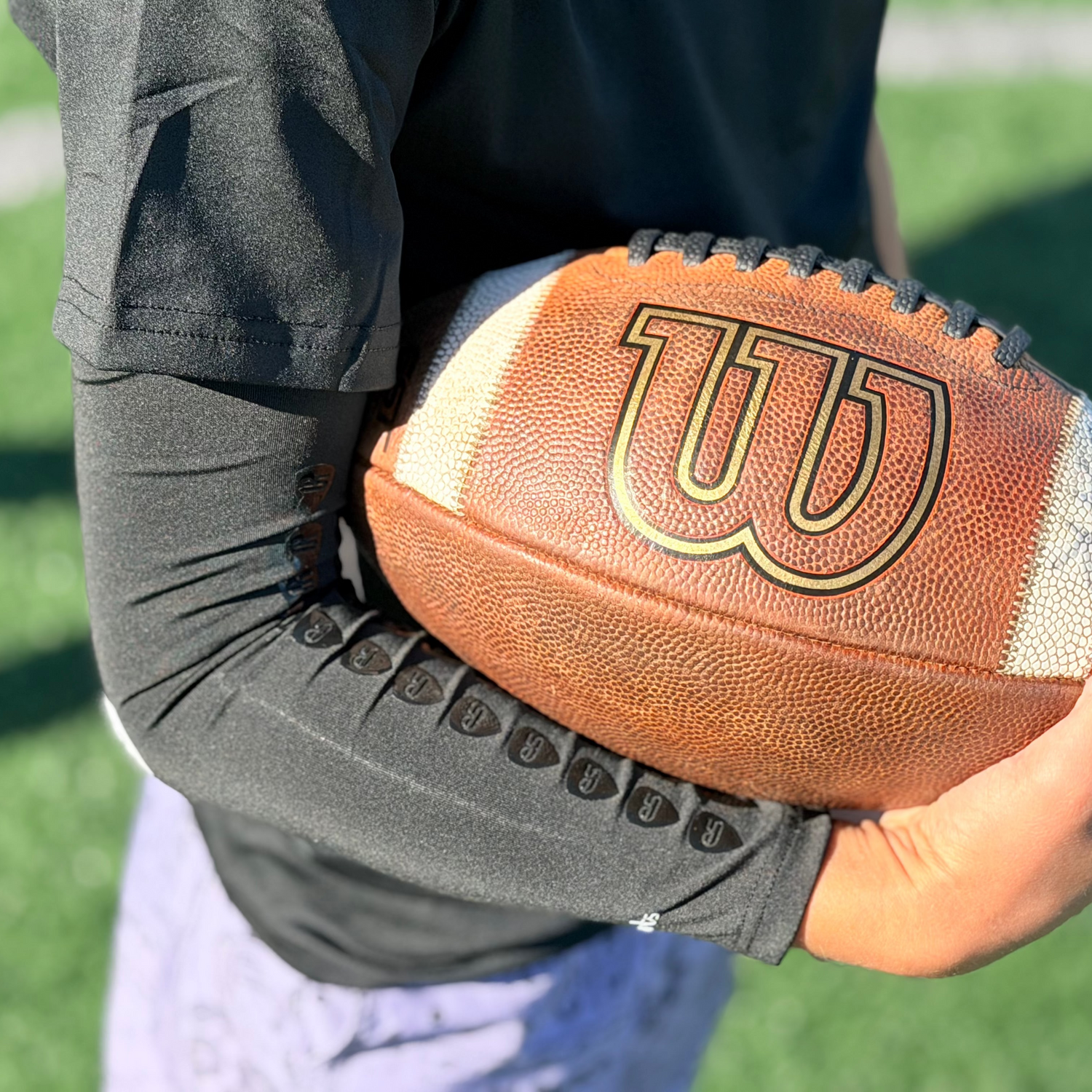 youth football player holding the ball on the grips off the compression arm sleeve